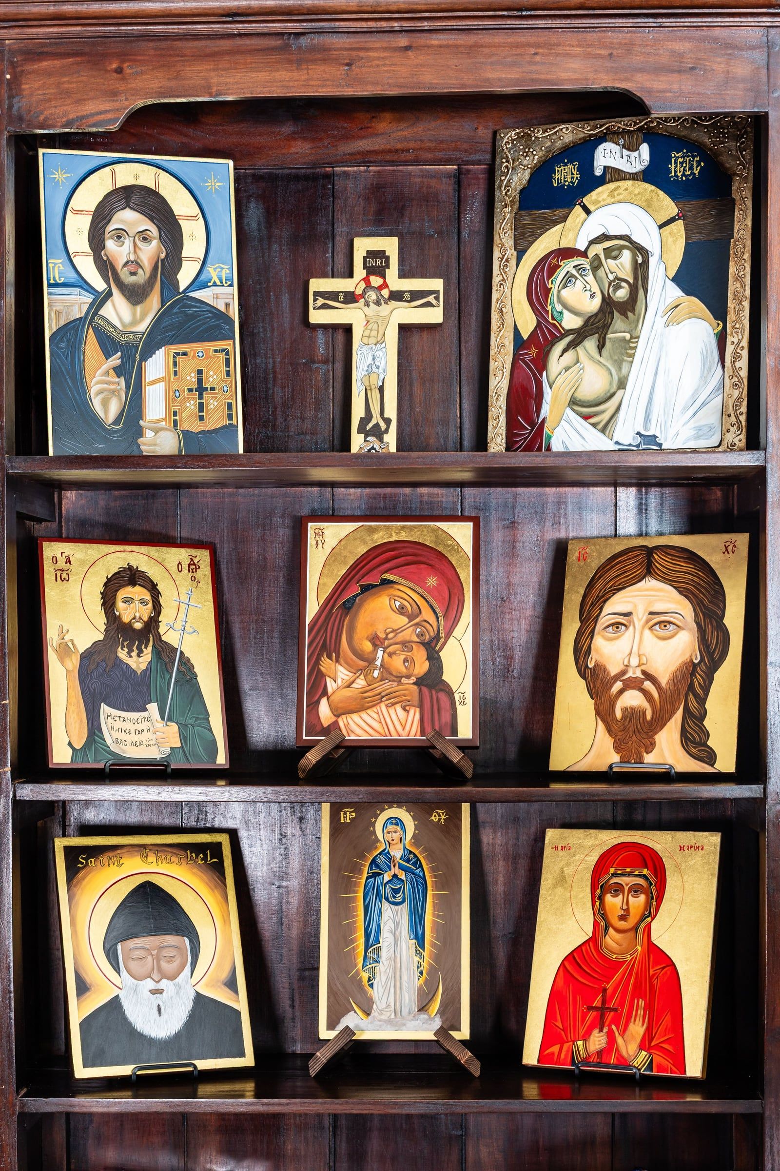 Une étagère de bois sombre garnie d'icônes de l'atelier : le Christ, la Mère de Dieu, des saints