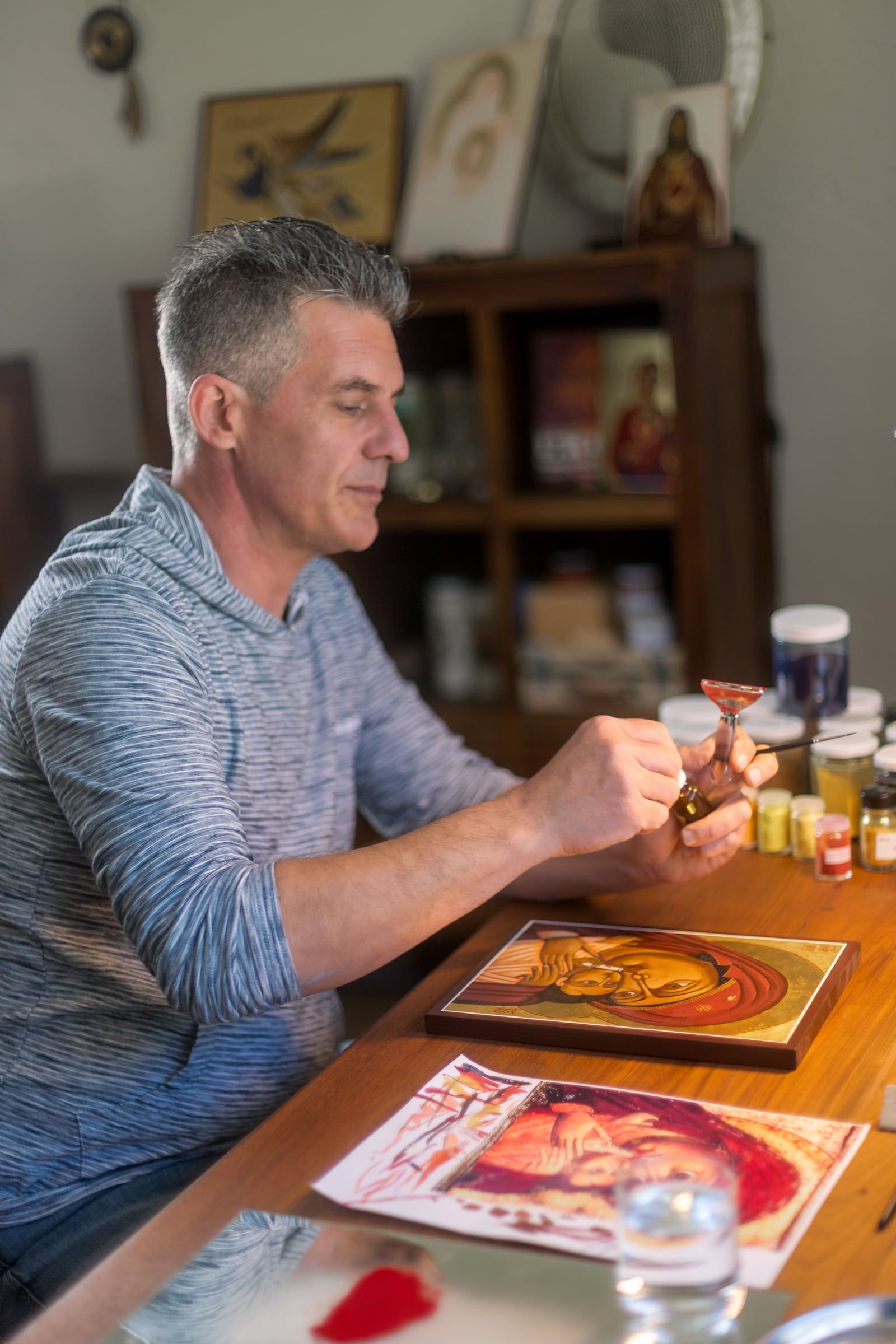 L'iconographe peint une icône à sa table de travail, entouré de pigments et d'autres icônes