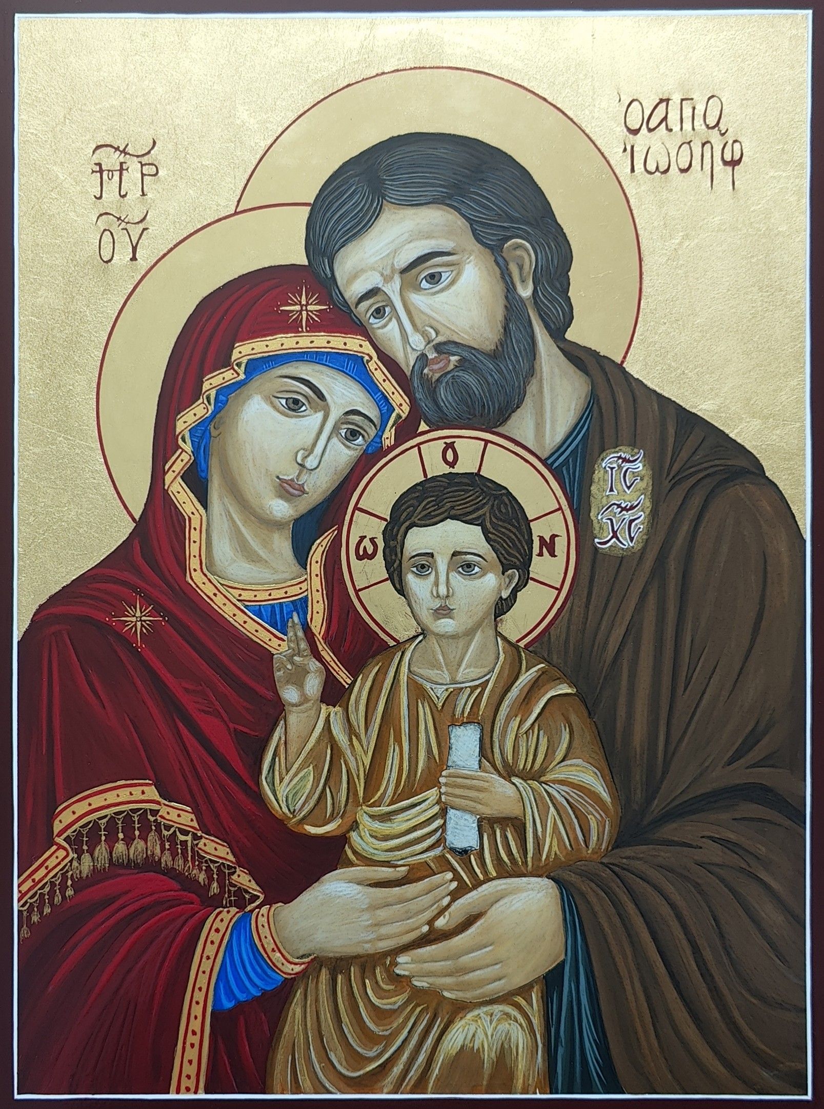 Icône de la Sainte Famille : la Mère de Dieu en maphorion rouge, saint Joseph en manteau brun et l'Enfant Jésus bénissant, tenant un rouleau, sur fond d'or, auréoles cerclées de rouge, cadre rouge foncé